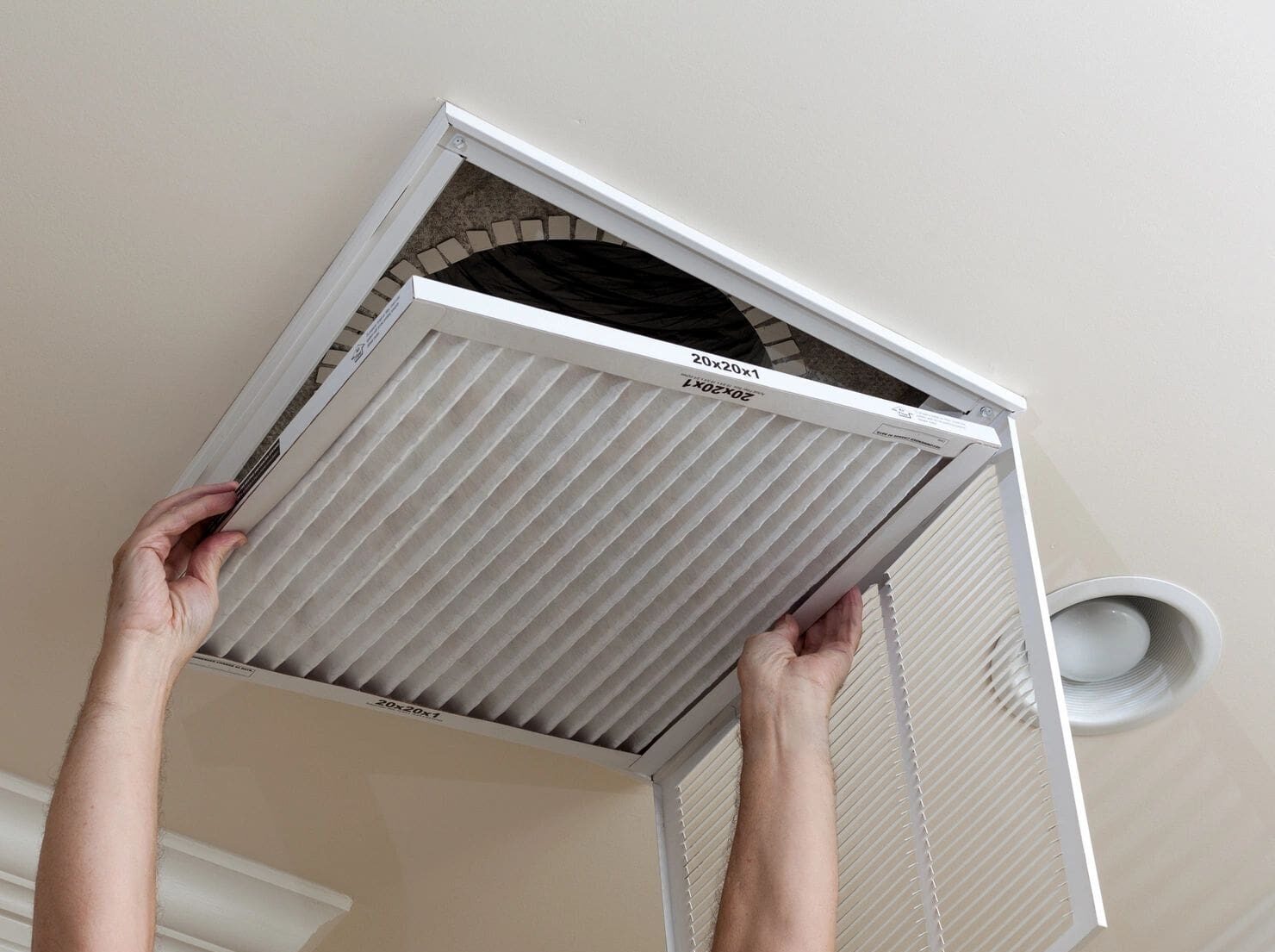 A person is holding an air filter in the ceiling.