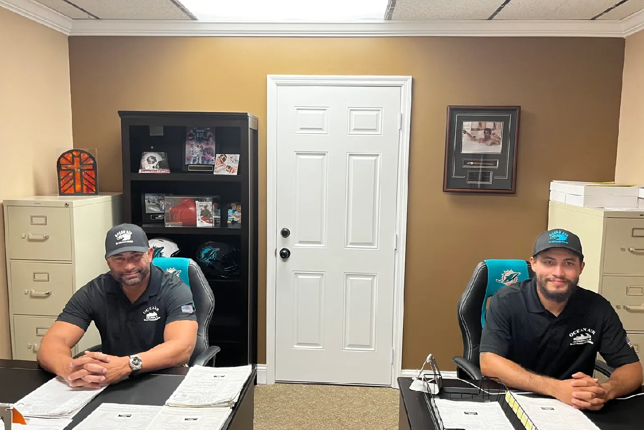 Two men sitting at a desk in front of an open door.